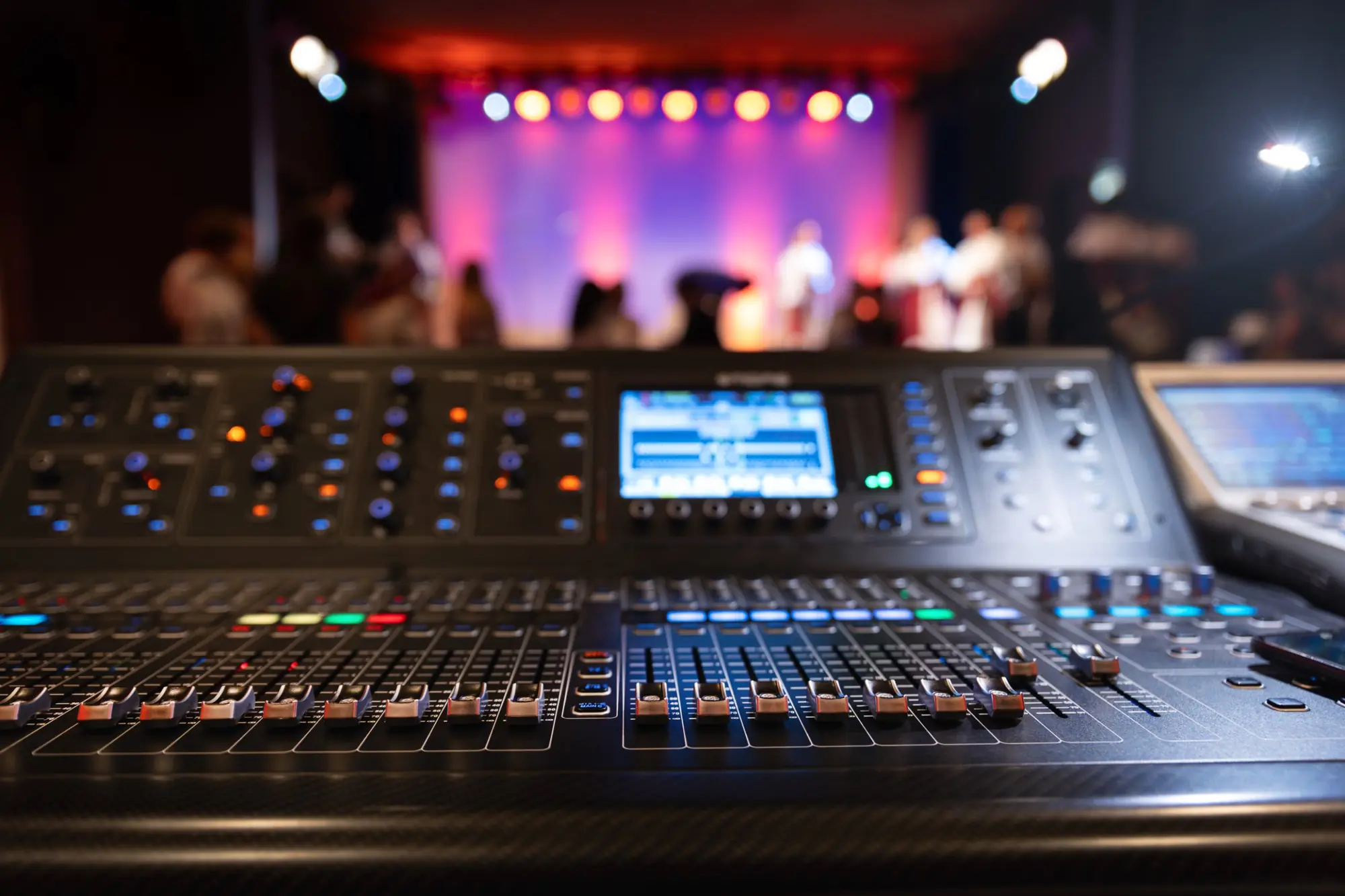 Digital mixing console at front of house facing a lit stage